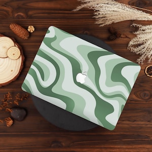 May include: A laptop skin featuring a wavy, abstract pattern in various shades of sage, forest, and pale green. The design covers the top surface of a laptop, incorporating a central cutout that reveals the silver Apple logo underneath.