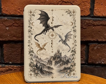 Può includere: Una custodia rettangolare per e-reader color crema con un'illustrazione dettagliata di tre draghi che volano sopra un castello e un lago. Il design include fasi lunari, stelle e un bordo floreale. La parola Nuvrae è stampata nell'angolo in basso.