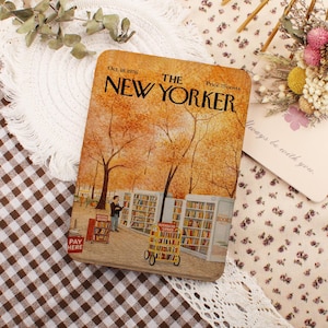 Könnte beinhalten: Ein rechteckiger Gegenstand mit einer Vintage-Cover-Illustration von "The New Yorker". Das Kunstwerk zeigt eine Herbstszene mit Bäumen, einer Bibliothek und Figuren. Der Text enthält "Oct. 18, 1976", "Price 75 cents" und "PAY HERE."