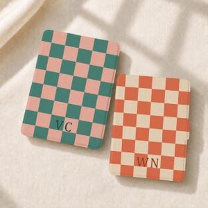 May include: Two rectangular e-reader cases featuring a checkered pattern. The larger case has a green and light pink checkerboard design with the letters VC printed in the center. The smaller case has an orange and cream checkerboard design with WN.
