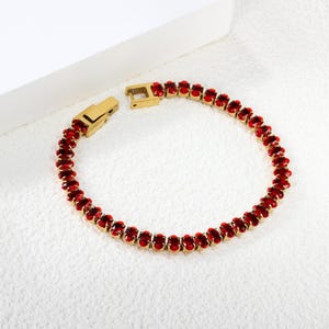 May include: Gold-toned bracelet featuring a series of oval-cut, vibrant red gemstones. The bracelet has a secure clasp and is displayed on a white surface. A piece of jewelry.