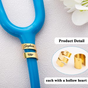 May include: A gold-coloured metal identification tag for a stethoscope, featuring the name Sophia and a leaf engraving. The product detail inset shows two gold-coloured metal tags, each with a small hollow heart shape cutout on the side.