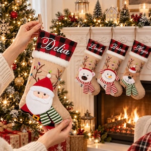 May include: A tan hessian Christmas stocking featuring a red and black buffalo check cuff with the name Delia embroidered in white. The stocking displays a plush Santa Claus applique with a green and white striped scarf and string light graphics.