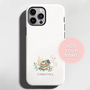 May include: White phone case with a floral design and the name "Christina" printed below a stack of books and playing cards. The case has a black camera module and a pink circle with the text "ADD YOUR NAME".