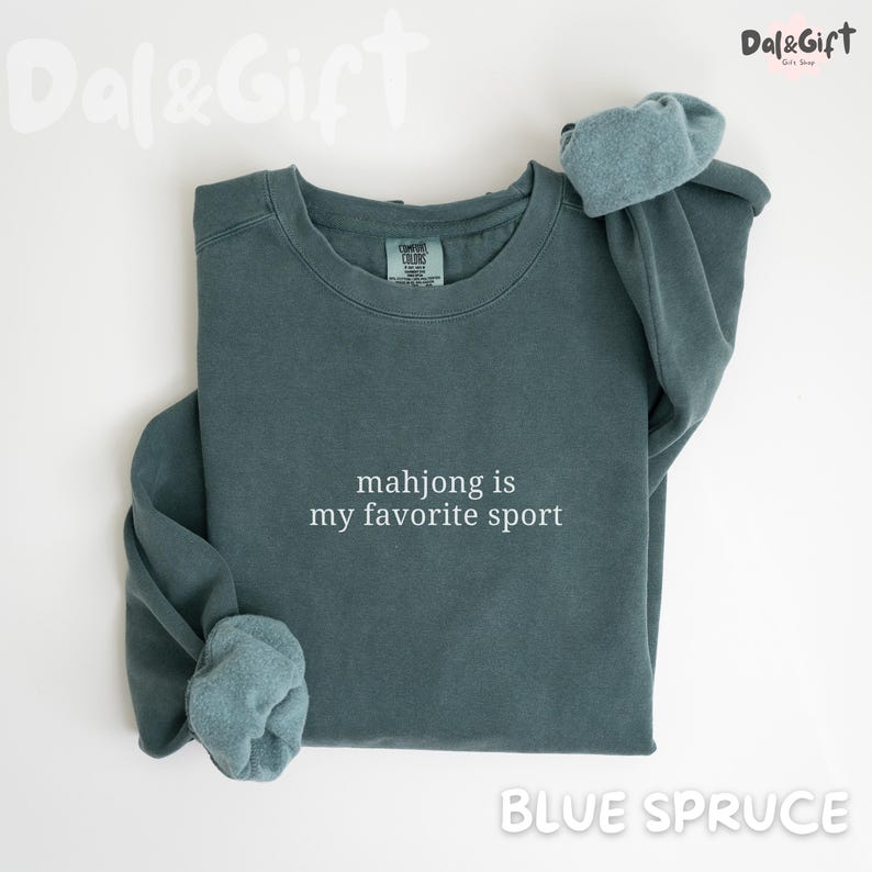 Pu&ograve; includere: Felpa blu abete con la scritta bianca "mahjong is my favorite sport". La felpa ha girocollo e maniche lunghe con polsini ripiegati. Il marchio "Dal&Gift" si trova nell'angolo in alto a destra.