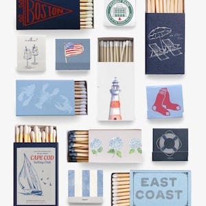 Könnte beinhalten: Eine Sammlung rechteckiger Streichholzschachteln mit verschiedenen Motiven, darunter ein Boston-Wimpel, das Fenway Park-Logo, ein Leuchtturm, ein Segelboot des Cape Cod Sailing Club, eine amerikanische Flagge, Hummer, rote Socken, Hortensien, ein Rettungsring und der Schriftzug East Coast.