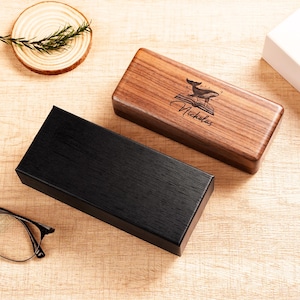 May include: Two rectangular boxes, one black and one wooden. The wooden box features a whale and book design with the name "Nicholas" engraved. The boxes are on a light wood surface.