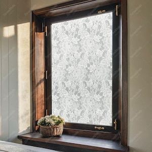 May include: A dark wood-framed window with a white lace pattern covering the glass. A small wicker basket with white flowers sits on the windowsill. The window is closed with brass hardware.