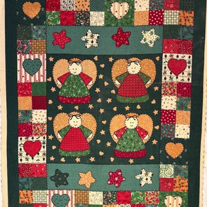 May include: A handmade quilt with a dark green background and a patchwork design. The quilt features four angel figures with gold wings and red and green dresses, surrounded by hearts and stars in various colors. The border is a patchwork of squares.