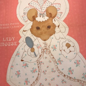 May include: A fabric panel featuring a charming illustration of Lady Mouse from Beatrix Potter's Nursery Classics. The mouse is depicted in a white dress with pink floral accents, holding a small mirror. The background is a soft pink with a dotted pattern.
