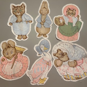 May include: A collection of six fabric appliqués featuring whimsical animal characters. The appliqués include a cat, rabbit, mouse, duck, and hedgehog, each dressed in vintage-style clothing. The color palette is soft, with pastel shades of blue, pink, and green.