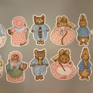 May include: A collection of whimsical die-cut stickers featuring various animal characters in vintage clothing. The stickers include cats, rabbits, and ducks, dressed in pastel colors with floral and patterned details. Ideal for scrapbooking and crafts.