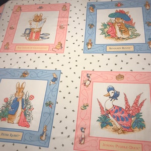 May include: A white fabric featuring four framed illustrations of Beatrix Potter characters: The Tailor of Gloucester, Benjamin Bunny, Peter Rabbit, and Jemima Puddle-Duck. Each illustration is surrounded by a pink or blue border with the character's name.