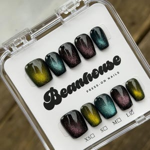 May include: A set of press-on nails in a clear plastic case. The nails have a glossy finish with a color-shifting effect, transitioning from dark purple to teal and yellow. The brand name "Beanhouse" is printed on the packaging.