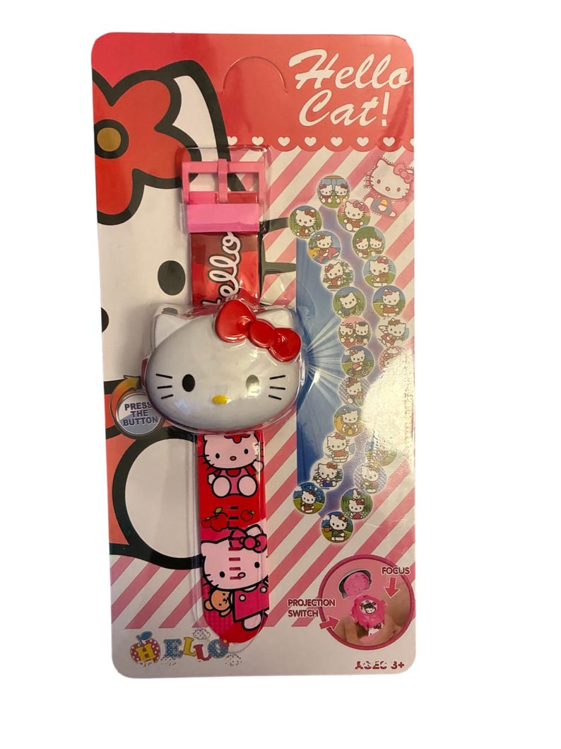 May include: A Hello Kitty watch on a pink and red card. The watch has a white face with a red bow and a red band with Hello Kitty images. The card reads "Hello Cat!" and has a projection switch.