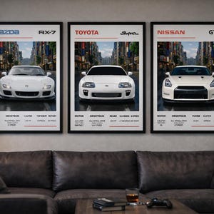 Puede incluir: Tres láminas enmarcadas de coches deportivos blancos: un Mazda RX-7, un Toyota Supra y un Nissan GT-R. Cada lámina incluye el nombre, el logotipo y las especificaciones del coche. Se exhiben sobre un sofá de cuero marrón oscuro.