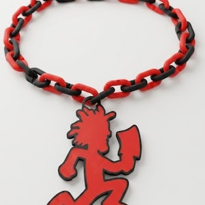 May include: A necklace featuring a chain of alternating matte black and bright red plastic links. A large, flat, red pendant shaped like a running figure holding a cleaver hangs from the center of the chain, outlined in a thin black border.