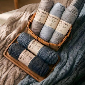 May include: A selection of wool thread skeins in shades of grey and blue, presented in a woven basket and a wooden tray. The labels read "WOOL THREAD Premium Soft and comfortable Not irritating."