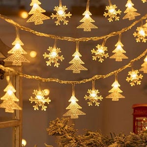 May include: A string of warm white Christmas lights with tree and snowflake shapes. The lights are strung on a thin, brown wire, creating a festive display. The lights are lit, creating a warm glow, perfect for the holiday season.
