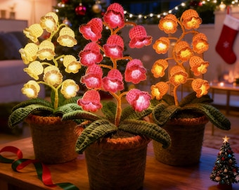 May include: Three decorative, illuminated floral arrangements in woven pots. The flowers are crocheted in yellow, red, and orange, with internal lights. Green leaves and stems complete the design. The arrangements sit on a wooden table, with a Christmas tree and decorations in the background.