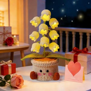 May include: A handcrafted crochet lamp shaped like lily of the valley flowers. The flowers are yellow with white edges and emit a warm glow. The lamp sits in a beige pot with a smiling face and brown feet. A charming decorative piece.