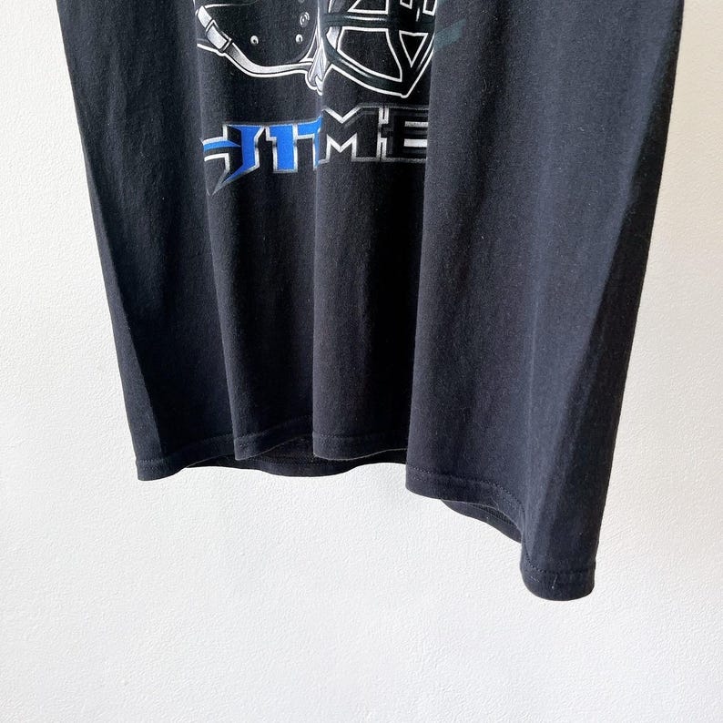 Puede incluir: Camiseta negra con un dise&ntilde;o gr&aacute;fico en blanco y azul. El dise&ntilde;o incluye la palabra "TIME" en una fuente estilizada. La camiseta est&aacute; hecha de un material suave y tiene un cuello redondo cl&aacute;sico.