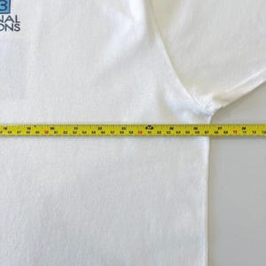 May include: A white t-shirt with the text "NAL ONS" in blue. A yellow measuring tape is laid across the shirt, showing measurements from 18 to 73 inches.