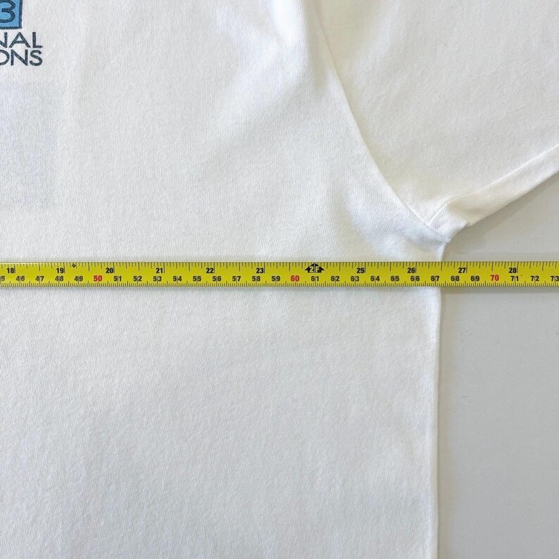 May include: A white t-shirt with the text "NAL ONS" in blue. A yellow measuring tape is laid across the shirt, showing measurements from 18 to 73 inches.