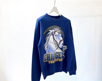 Puede incluir: Sudadera azul marino con un gráfico de cabeza de caballo blanco y brida marrón. El texto "CHARGERS SAN DIEGO" es dorado. Un rayo dorado está encima de la cabeza del caballo. También se ven las palabras "SUNDAY NIGHT FOOTBALL".
