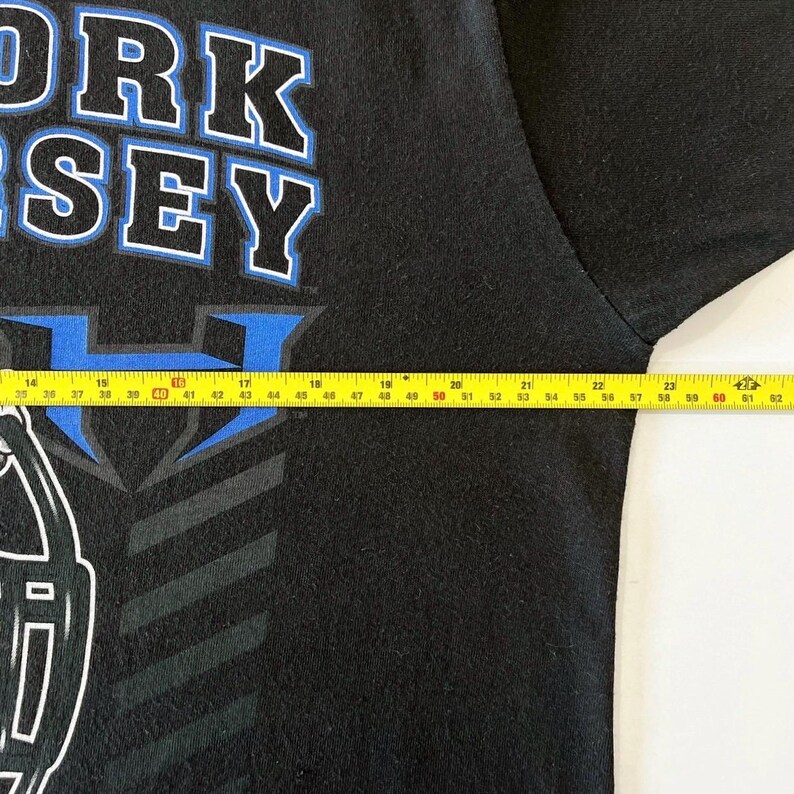 Puede incluir: Camiseta negra con el texto "ORK SEY" en blanco y azul. Una cinta m&eacute;trica se coloca sobre la camiseta, mostrando medidas en cent&iacute;metros. La camiseta tiene un dise&ntilde;o gr&aacute;fico en la parte inferior izquierda.