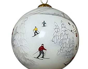 Puede incluir: Adorno navideño blanco con una escena de esquí invernal. El adorno presenta esquiadores con chaquetas amarillas y rojas, árboles nevados y un telesilla. Un lazo dorado en la parte superior para colgar. El diseño está pintado a mano.
