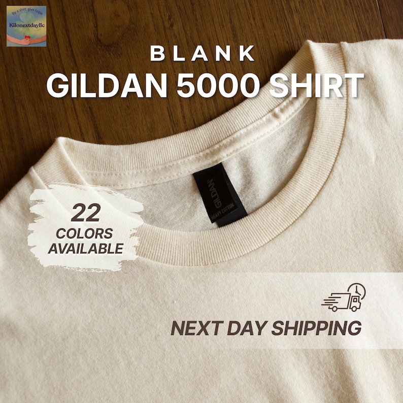 May include: Cream-colored Gildan 5000 shirt with a crew neck. The shirt has a black tag and the text "BLANK GILDAN 5000 SHIRT". The image also includes the text "22 COLORS AVAILABLE".