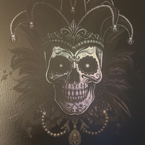 May include: A detailed illustration of a skull wearing a jester's hat and a jeweled necklace. The skull is white with intricate designs, set against a dark background. Feathers and pearls add to the decorative elements.