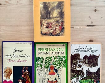 Könnte beinhalten: Eine Sammlung von Jane Austen-Klassikern, darunter "Emma", "Sense and Sensibility", "Persuasion" und "Northanger Abbey". Die Bücher haben farbenfrohe Einbände mit Illustrationen und Text auf einer hellen Holzoberfläche.