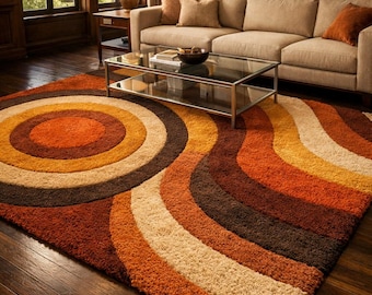 Puede incluir: Una alfombra de estilo retro con un diseño circular en tonos naranja, marrón y beige. La alfombra está colocada sobre un suelo de madera oscura en un salón, con un sofá y una mesa de centro visibles en el fondo.