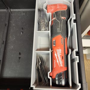 Puede incluir: Una herramienta angular inalámbrica Milwaukee FUEL M12 roja y negra con accesorios, almacenada en una bandeja organizadora gris dentro de una caja de herramientas negra. La herramienta tiene el logotipo de Milwaukee y la marca FUEL.