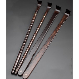 Puede incluir: Cinco rascadores de espalda de madera marrón oscuro con diferentes diseños de mango. Uno tiene un mango con cuentas, otro un mango estilo bambú, y los otros son planos con un extremo curvo. Cada uno tiene una cabeza rascadora rectangular.