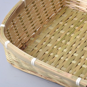 Könnte beinhalten: Ein rechteckiger Korb aus geflochtenem Bambus. Der Korb besteht aus dünnen, hellbraunen Bambusstreifen, die in einem Kreuzmuster kunstvoll geflochten sind. Die Kanten sind abgerundet und mit weißer Schnur verstärkt. Der Korb ist leer.