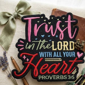 May include: Embroidered patch with the text "Trust in the Lord with all your heart" in pink, red, and blue. The patch is on a black background with a decorative border. The patch also includes the text "Proverbs 3:5".