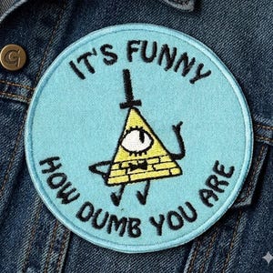 May include: A round, light blue embroidered patch with the text "IT'S FUNNY HOW DUMB YOU ARE" in black. The patch features a yellow triangle with an eye and a black top hat, and a black arm. The patch is on a blue denim jacket.