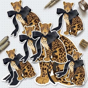 May include: A collection of leopard stickers with black bows. The stickers feature a leopard print pattern in shades of brown and tan. Each leopard has a black bow tied around its neck. The stickers are on a white background with small gray dots.