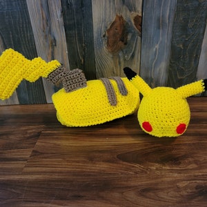 May include: A yellow crocheted Pikachu hat and a matching tail. The hat has black ears and red cheeks.