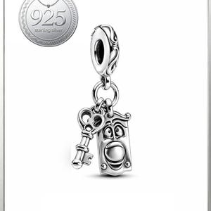 May include: A silver charm with a key and a door knocker design. The door knocker has a smiling face. The charm is attached to a decorative bail. A circular emblem with the text "925 sterling silver" is in the upper left corner.