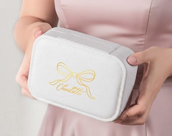 May include: A rectangular white jewelry box with a hinged lid. The front of the box features a gold-colored graphic of a ribbon bow and the name Charlotte written in a cursive script font. The box has a textured finish and rounded corners.