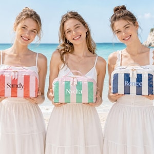 May include: Three rectangular toiletry bags with top handles and zipper closures. The left bag is pink and white striped with the name Sandy. The center bag is green and pink striped with the name Nydia. The right bag is blue and white striped with the name Renee.