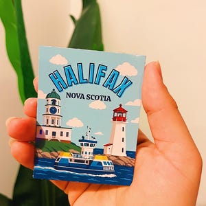 Può includere: Una carta rettangolare con un cielo azzurro, nuvole bianche e il testo HALIFAX NOVA SCOTIA. L'illustrazione raffigura due fari su coste rocciose e un traghetto blu e giallo sull'acqua con la parola HALIFAX scritta sulla fiancata.