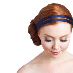 May include: A woman with red hair wearing a navy blue headband. Her hair is styled in a bun and she is looking down.