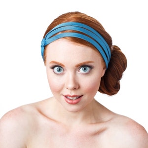 May include: A woman with red hair wearing a blue headband. She is looking at the camera with a surprised expression.