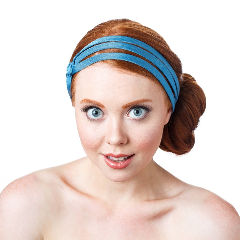 May include: A woman with red hair wearing a blue headband. She is looking at the camera with a surprised expression.