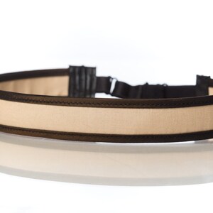 May include: A beige headband with black trim. The headband is made of a soft, comfortable fabric and has a subtle sheen.